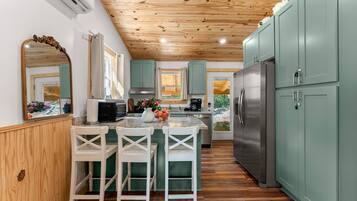Une cuisine avec un plafond en bois, des armoires vertes, un réfrigérateur en acier inoxydable et un coin bar avec des chaises blanches.