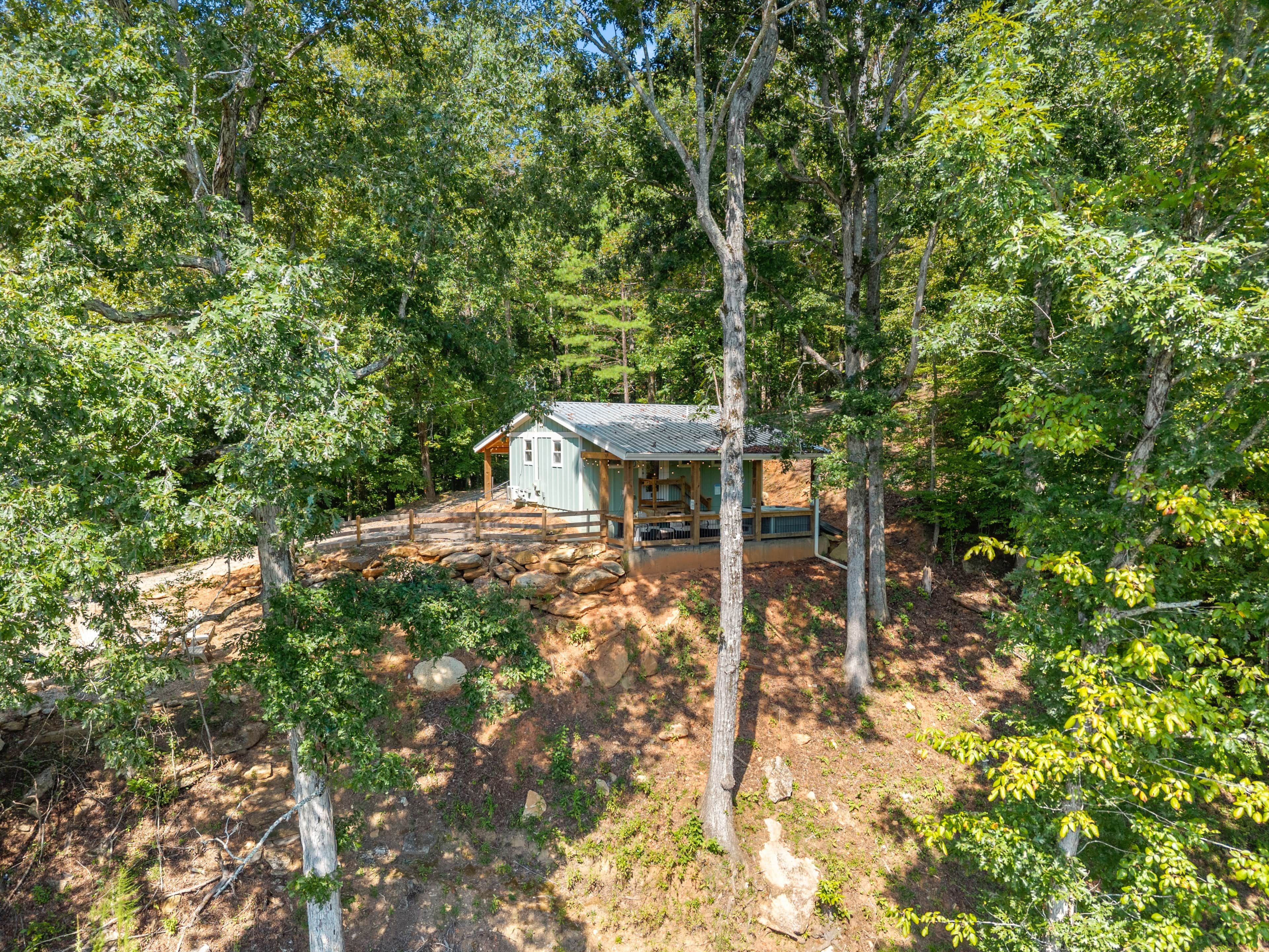 A cabin surrounded by trees, with a wooden deck and a stone pathway leading to it.