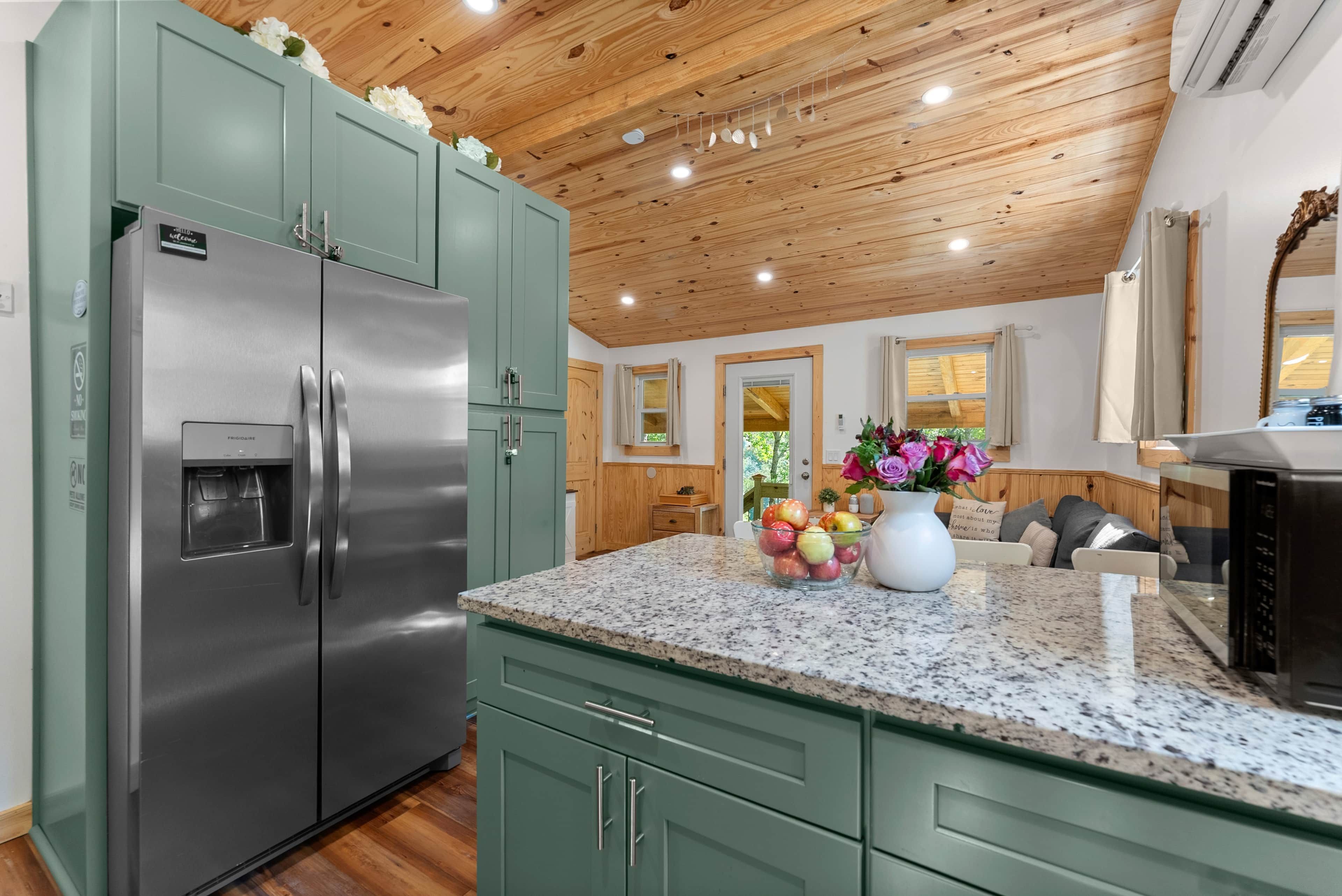 A kitchen with a stainless steel refrigerator, granite countertop, and wooden ceiling.