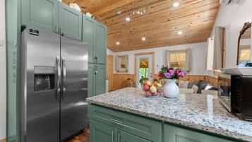 A kitchen with a stainless steel refrigerator, granite countertop, and wooden ceiling.