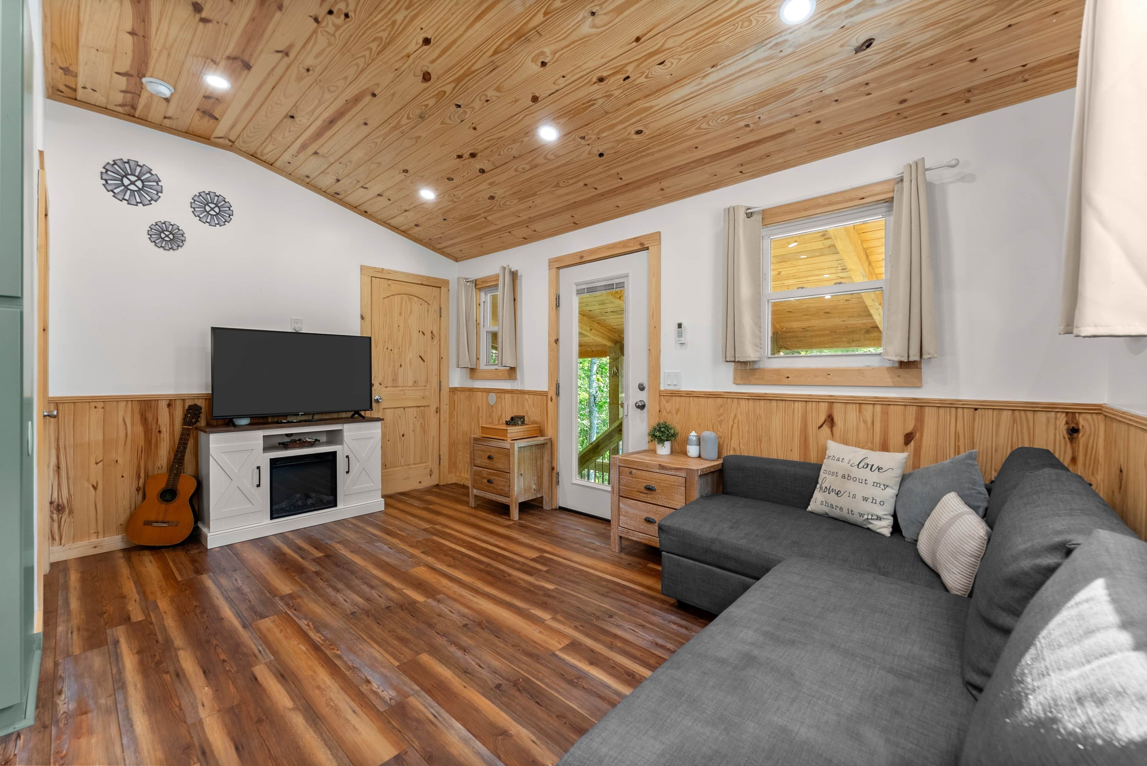 A cozy living room with a TV, wooden flooring, a couch, and a guitar.
