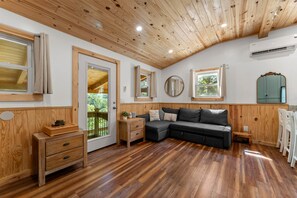 A room with wooden flooring, a sofa, a wooden cabinet, and a door leading to an outdoor area. - River Retreat Cabin (Cleveland)