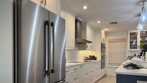 A modern kitchen with stainless steel appliances, white cabinetry, and a wooden floor.