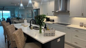 A modern kitchen with a central island, stainless steel appliances, pendant lighting, and a view to the outside.