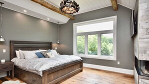 Une chambre à coucher avec un grand lit, un plancher en bois, une fenêtre donnant sur les arbres et un lustre.