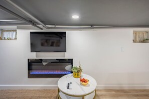 Une pièce dotée d’un téléviseur à écran plat fixé au mur, d’une cheminée en dessous et d’une table ronde sur laquelle se trouve un panier de fruits.