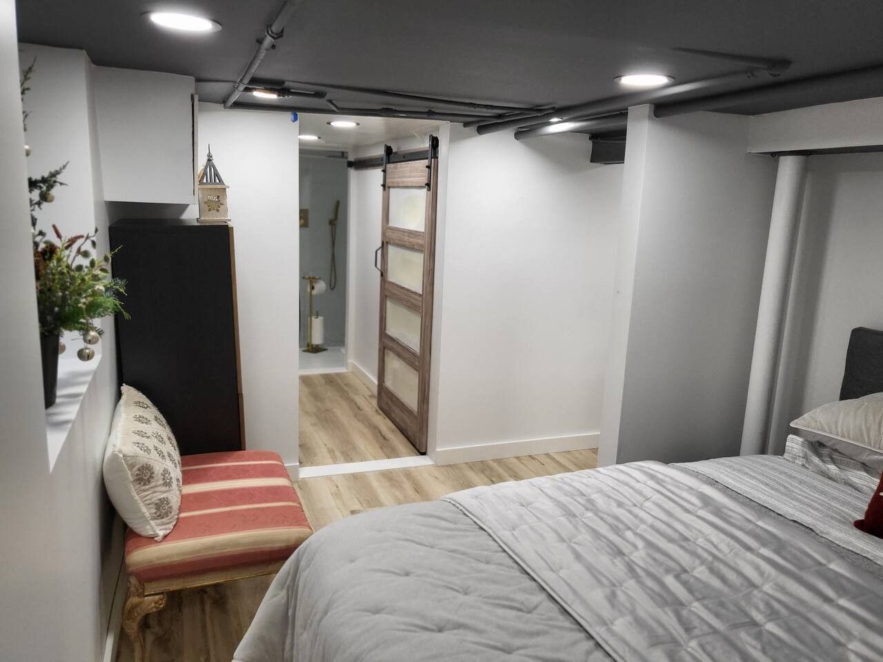 A bedroom with a bed, a bench, a door, and a small plant.