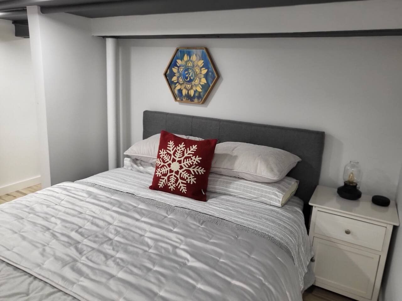 A bedroom with a bed, a nightstand, a decorative wall piece, and a small table with a lamp.
