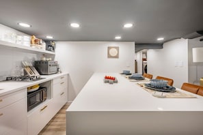 A modern kitchen with white cabinetry, a central island, and a dining area with chairs. - Romantic hideout. 1Br. Lower Level (Stamford)