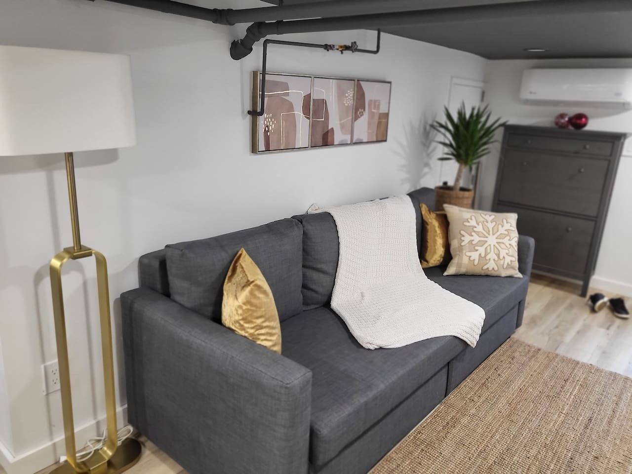 A modern living room with a grey sofa, a white throw blanket, and decorative pillows.