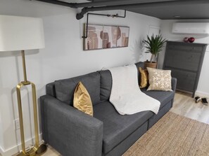 Un salon moderne avec un canapé gris, un plaid blanc et des coussins décoratifs.
