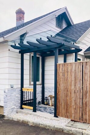 A house with a covered porch, a wooden fence, and a stone wall. - Romantic hideout. 1Br. Lower Level (Stamford)