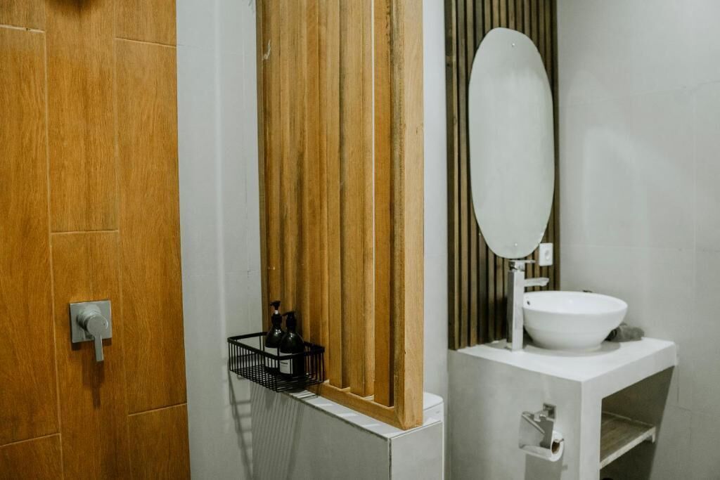 Une salle de bain avec une porte en bois, un lavabo blanc et un miroir.
