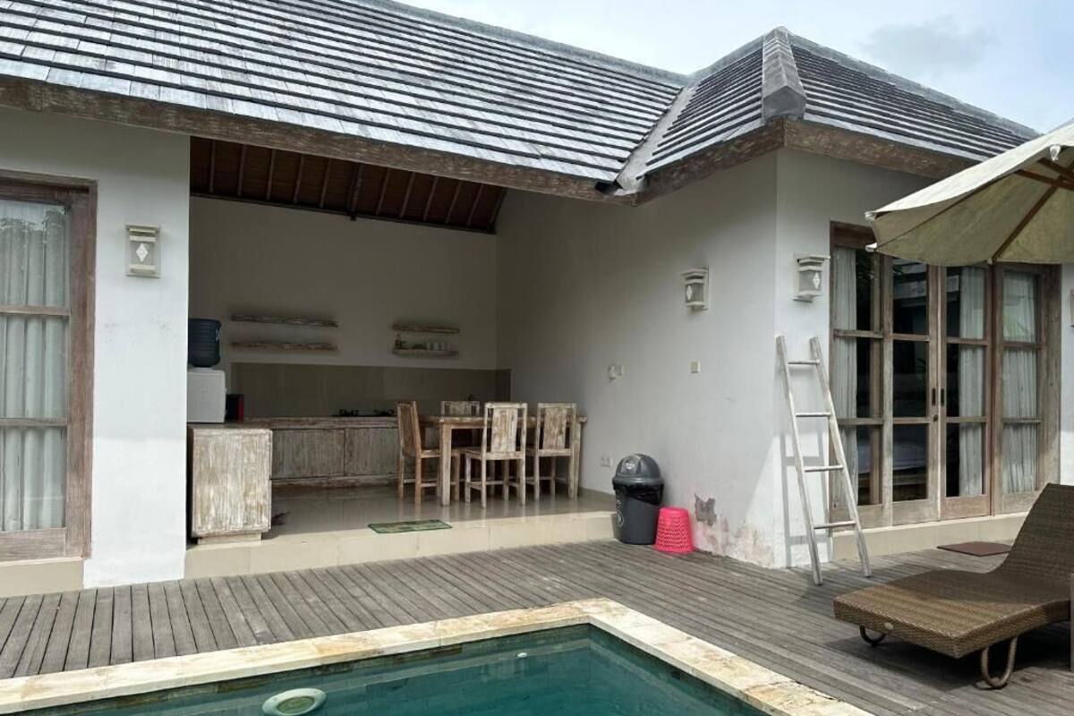 A poolside area with a wooden deck, a lounge chair, and a covered seating area.