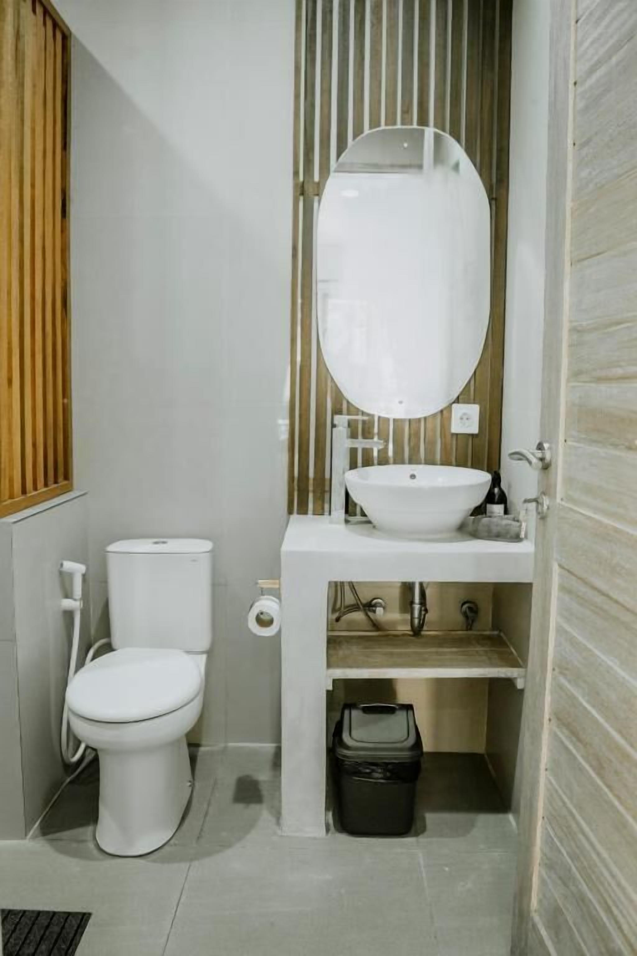 A compact bathroom with a white toilet, a white sink with a mirror above, and a black trash bin underneath.