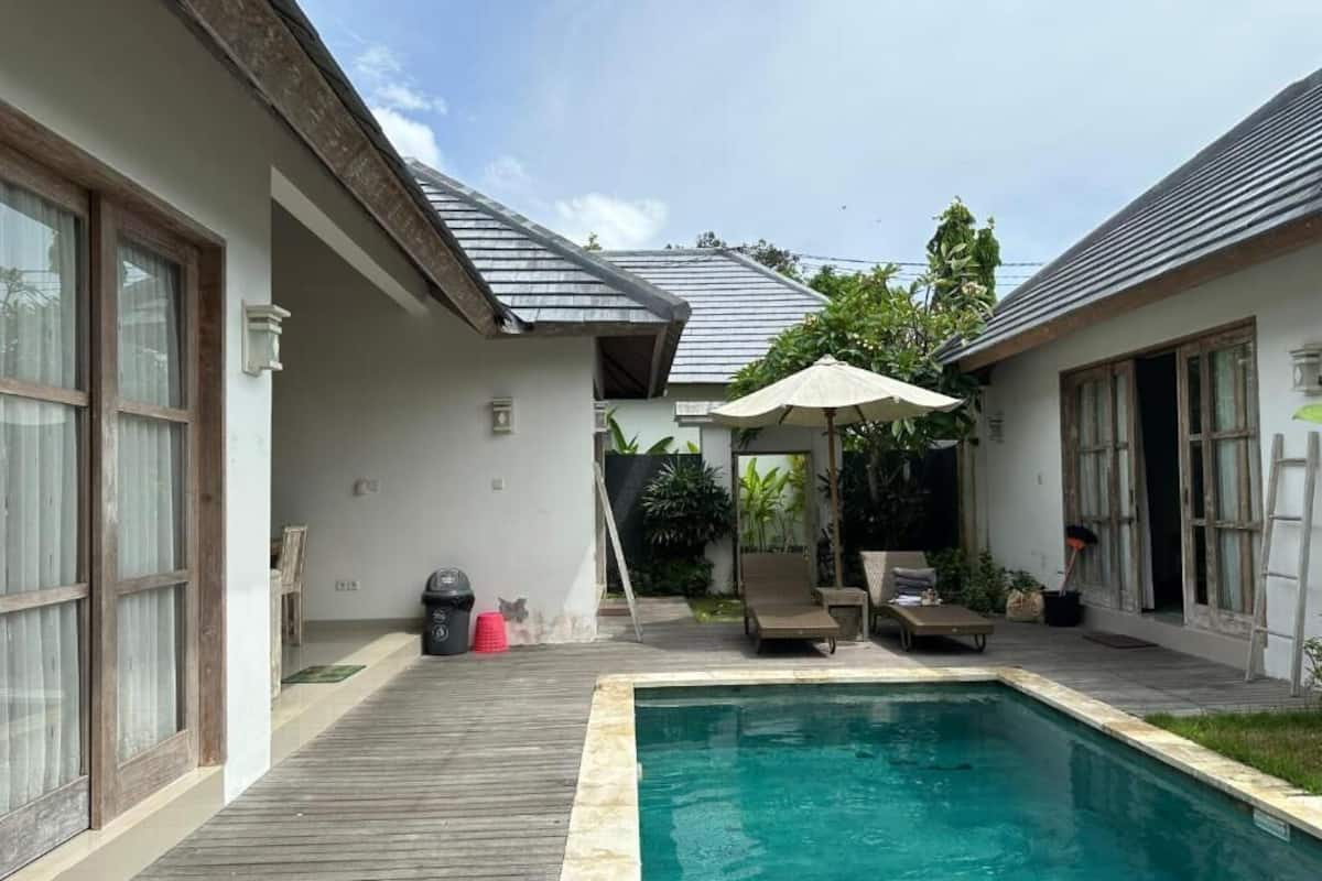 A pool area with a wooden deck, lounge chairs, and a covered seating area.