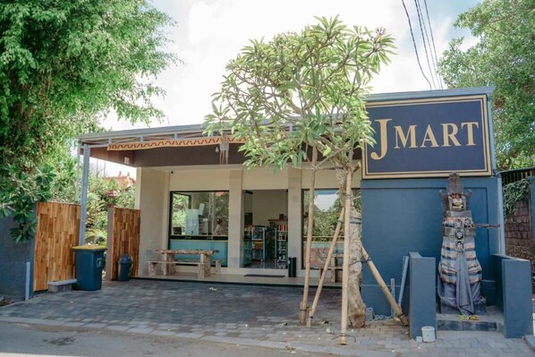 Un pequeño local moderno con un letrero 'Jmart', un área de estar cubierta y una estatua en el exterior.