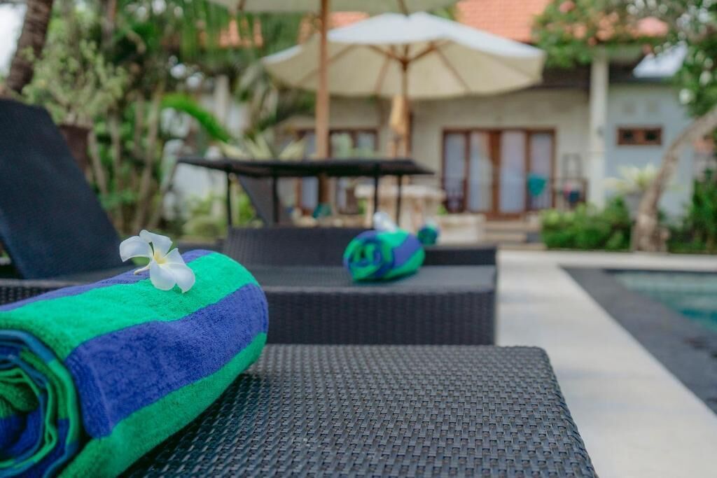 A poolside area with a lounge chair, a rolled towel, and a flower.