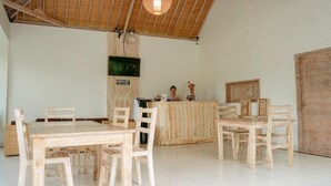 A reception area with a wooden reception desk, several wooden chairs, a large wooden door, and a ceiling with exposed beams. - Bingin Garden Uluwatu (Pecatu)