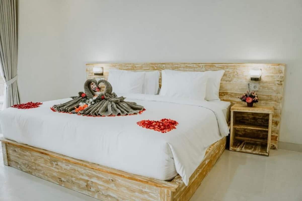 A bed with a wooden headboard, white bedding, and a decorative pillow arrangement with red flowers.