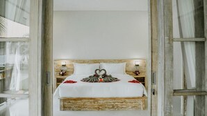 A bed with a heart-shaped decoration made of flowers and feathers, white bedding, and wooden headboard. - Bingin Garden Uluwatu (Pecatu)