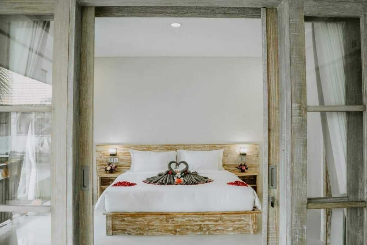 A bed with a heart-shaped decoration made of flowers and feathers, white bedding, and wooden headboard.