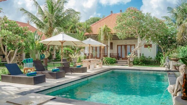 A pool area with lounge chairs and umbrellas, surrounded by tropical plants and a building with a tiled roof. - Bingin Garden Uluwatu (Pecatu)