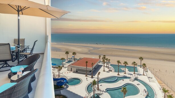 A balcony with a view of a beach and a pool area.