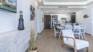 A modern kitchen with white cabinets, a dining area with white chairs, and a living area with a TV and decorative items.