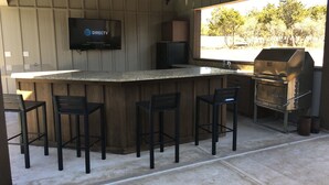 An outdoor kitchen area with a bar, seating, a television, and a grill. - Welcome to Little Blanco! Bonus: Free Golf During Your Stay! (Concan)