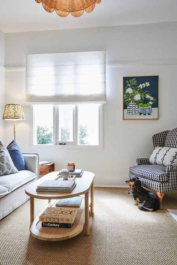 A cozy living room with a sofa, a striped armchair, a round coffee table with books, a lamp, and a painting on the wall.