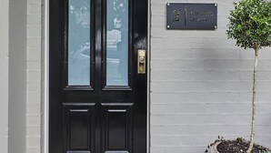 A black double door with a glass panel, a small potted plant, and a wall-mounted light fixture.