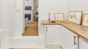 A kitchen with white cabinets, a wooden countertop, and a sink. There are framed pictures on the wall and a rug on the floor.