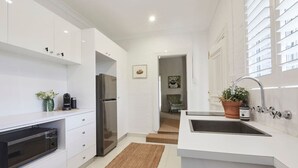 A modern kitchen with white cabinetry, a built-in oven, a stainless steel refrigerator, and a sink with a potted plant.