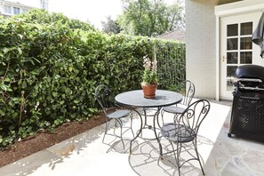 A patio with a round metal table and chairs, surrounded by a hedge and a white building. - Little Terrace Bowral 1 (Bowral)