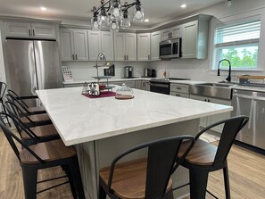 A modern kitchen with white cabinetry, stainless steel appliances, and a large marble island with bar stools.