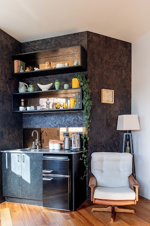A compact kitchen with dark cabinetry, a built-in refrigerator, and a wooden chair.