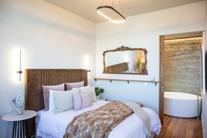 A bedroom with a bed, bedside table, wall-mounted mirror, and a built-in bathtub. - The Verdict Suite (Martinborough)