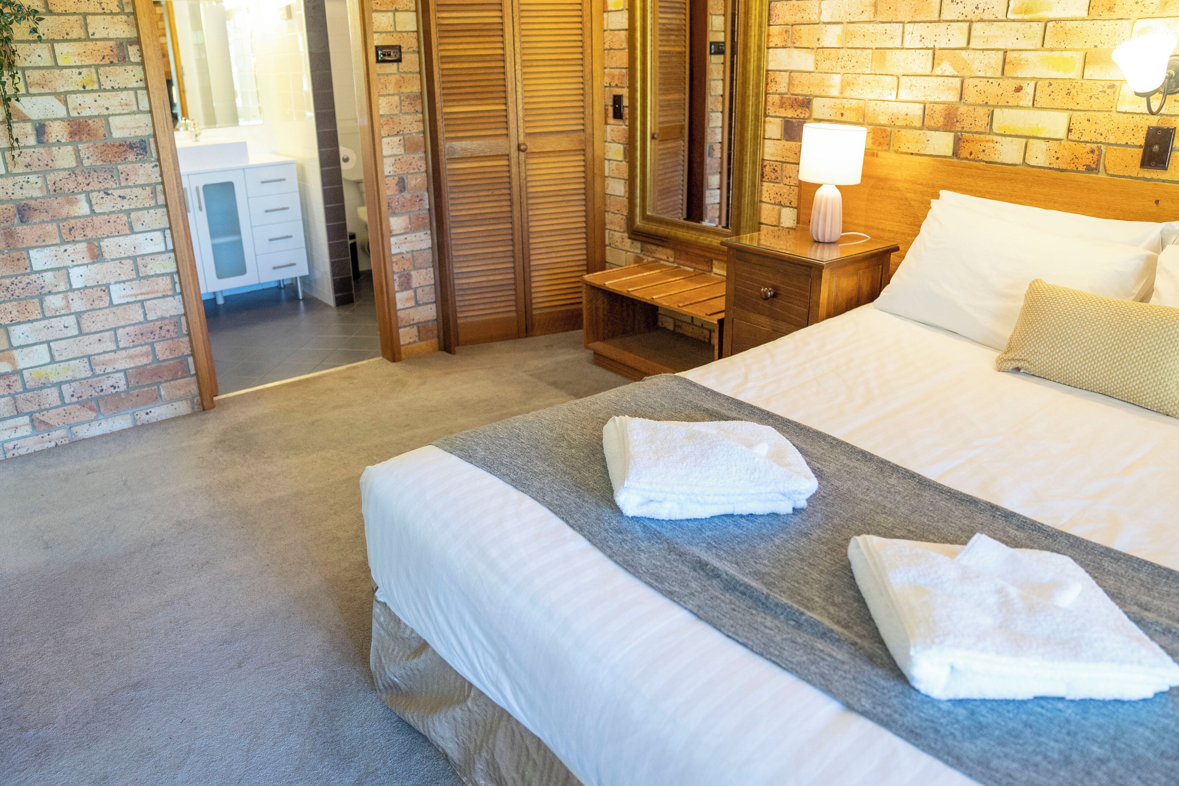 Habitación de hotel con una cama grande, una mesita de noche de madera, un espejo y una pared de ladrillo.