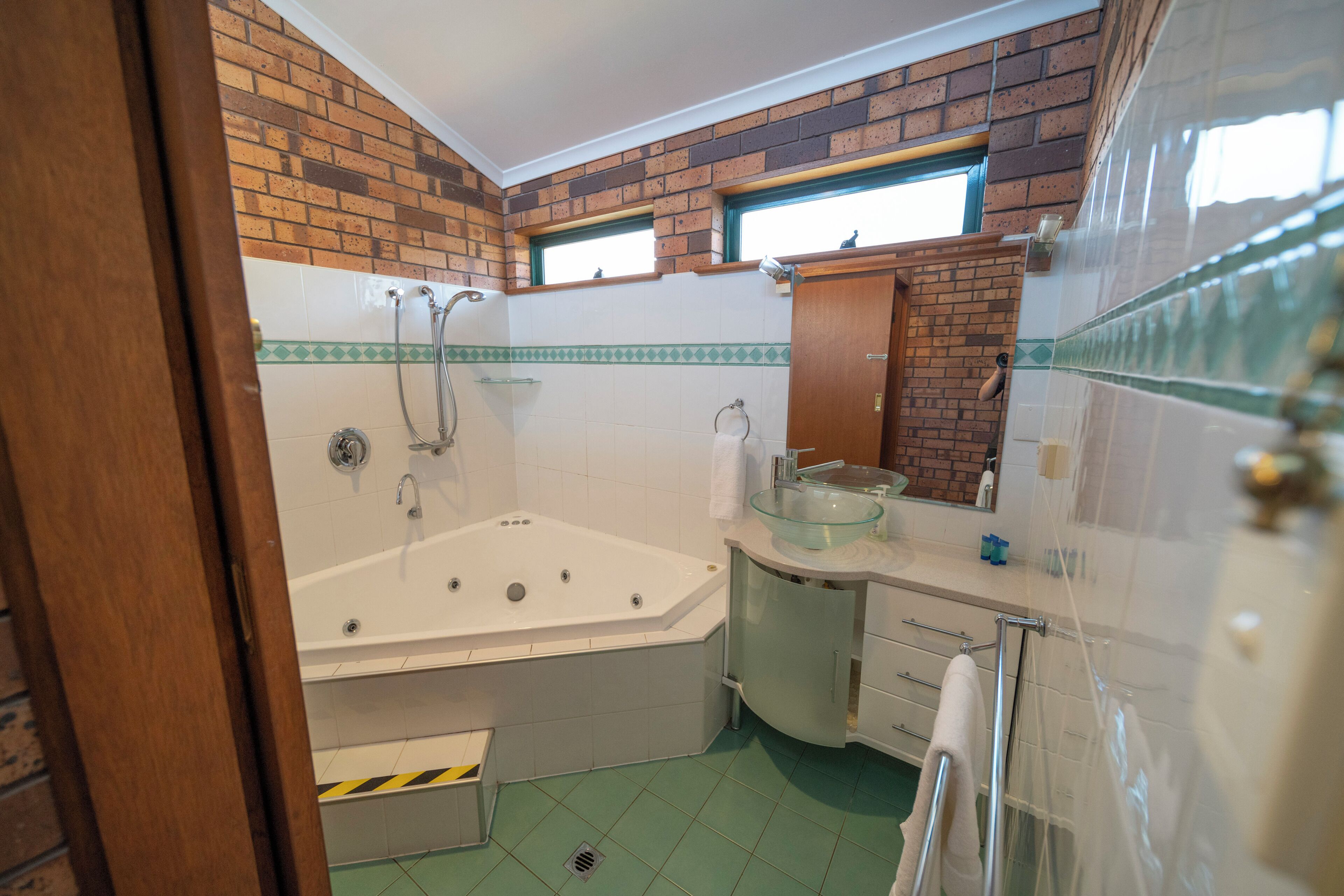 Een badkamer met een bad, een wastafel met glazen ombouw en een spiegel boven de wastafel.