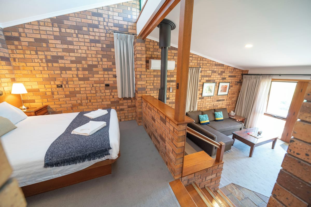 A hotel room with a brick wall, a bed with towels, a sofa, a table, and a fireplace.