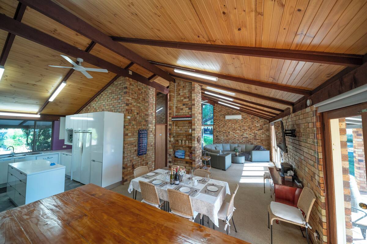 A spacious kitchen with white appliances, a dining area with a wooden table, and a brick wall.