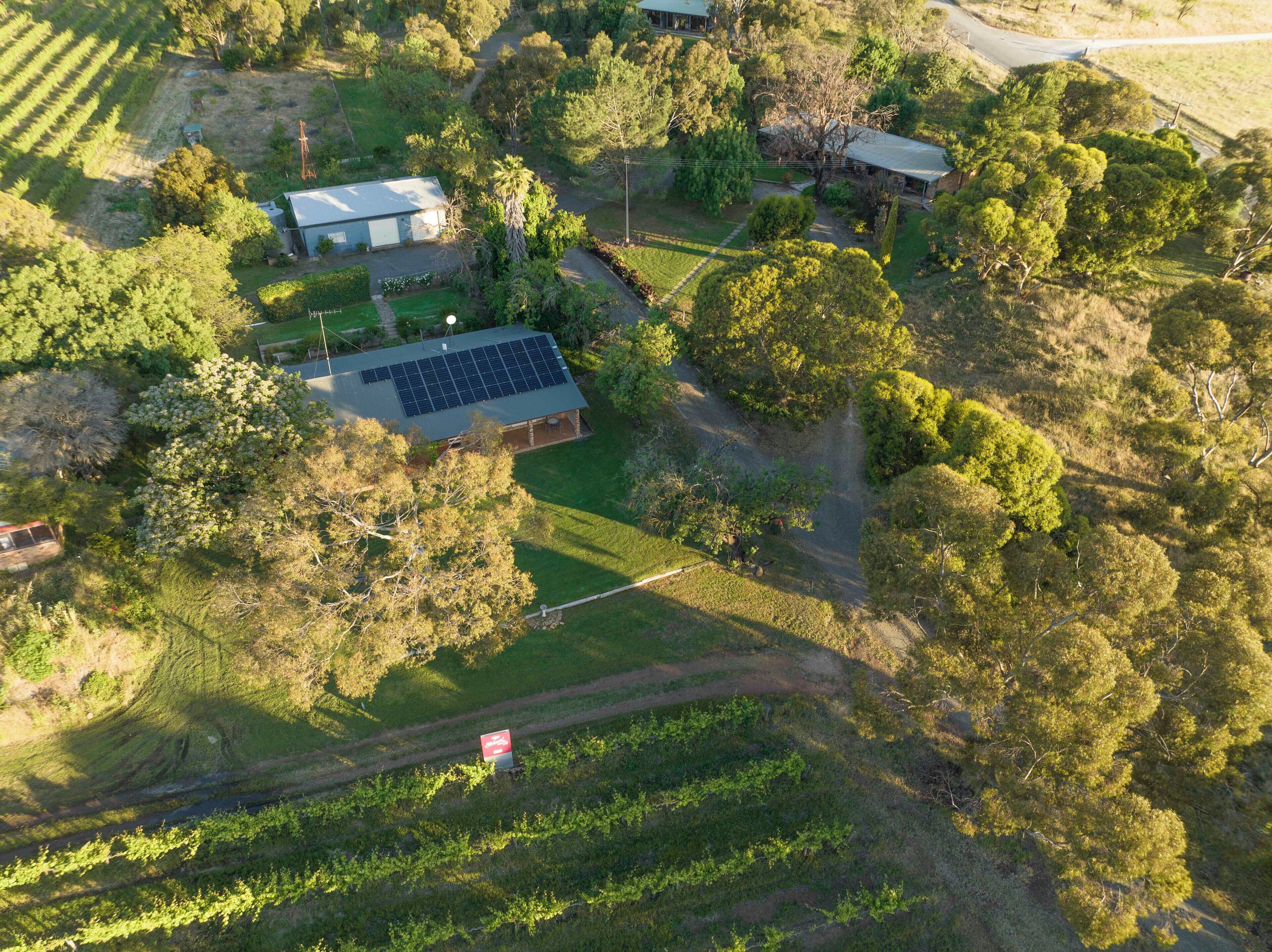 An aerial view of a property with a house, solar panels, and surrounding greenery.