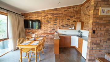 A dining area with a brick wall, a TV mounted above the counter, and a kitchen with white cabinets and a brick backsplash.