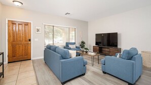 A living room with two blue sofas, a coffee table, a TV, and a wooden door. - Spacious 6-bedroom 3 Bathroom Entire House in charming Gilbert Sleeps 12 (Gilbert)