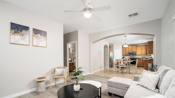 A spacious living room with a sofa, a round table with a plant, a ceiling fan, and a view into the kitchen area. - Spacious 6-bedroom 3 Bathroom Entire House in charming Gilbert Sleeps 12 (Gilbert)