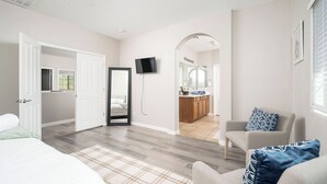 A modern bedroom with a large bed, a sitting area with a chair and a small table, a mirror, and a view into the bathroom. - Spacious 6-bedroom 3 Bathroom Entire House in charming Gilbert Sleeps 12 (Gilbert)