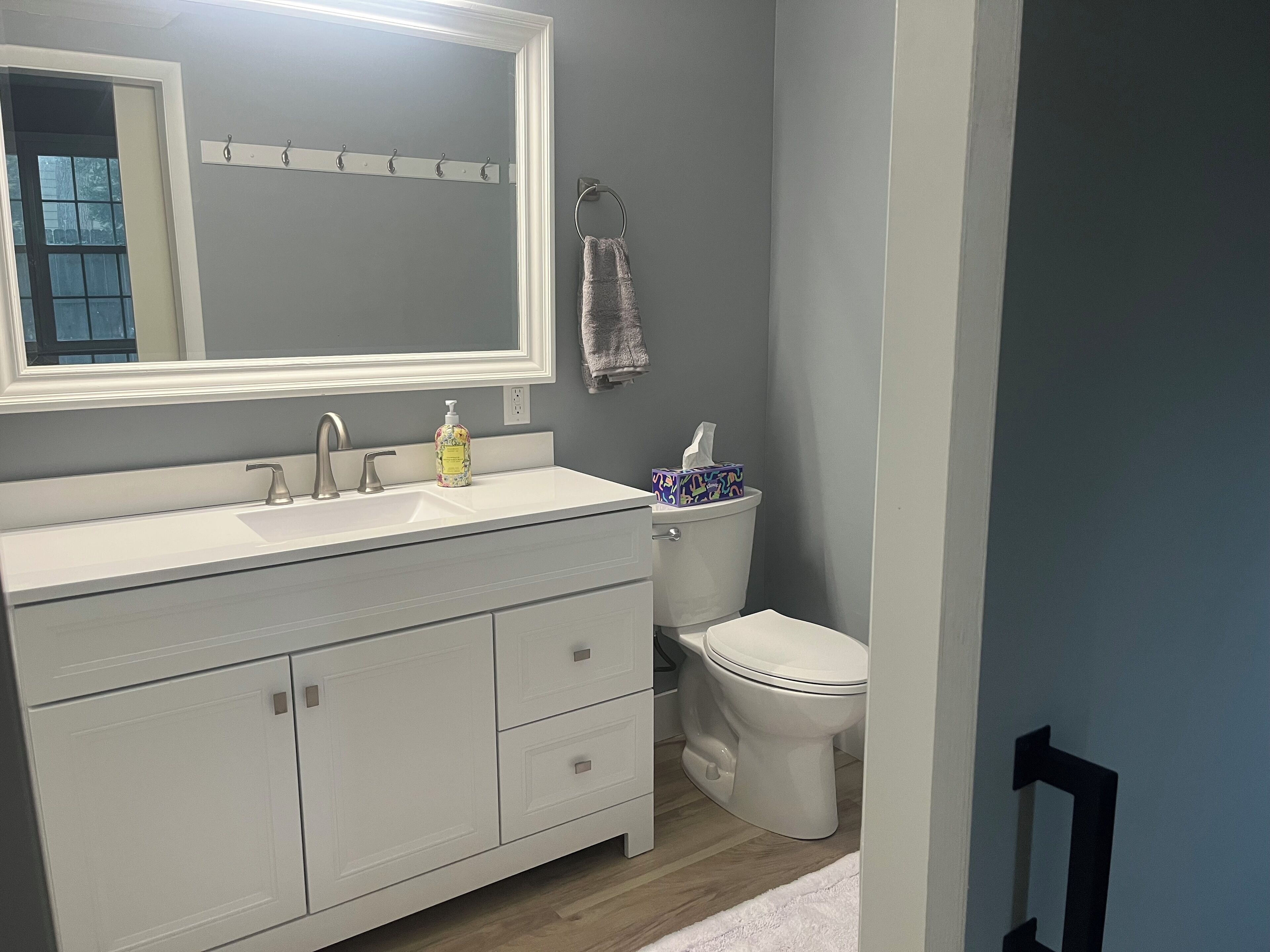 Een badkamer met een wit wastafelmeubel, een grote spiegel, een toilet en een handdoek aan de muur.