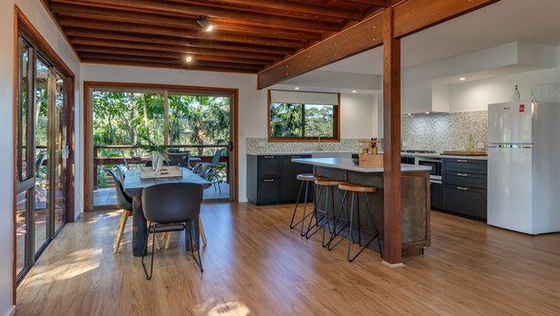 A modern kitchen with a central island, bar stools, and a dining area with a table and chairs.