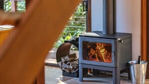 A wood-burning stove with visible flames, a metal bucket, and a stack of firewood.